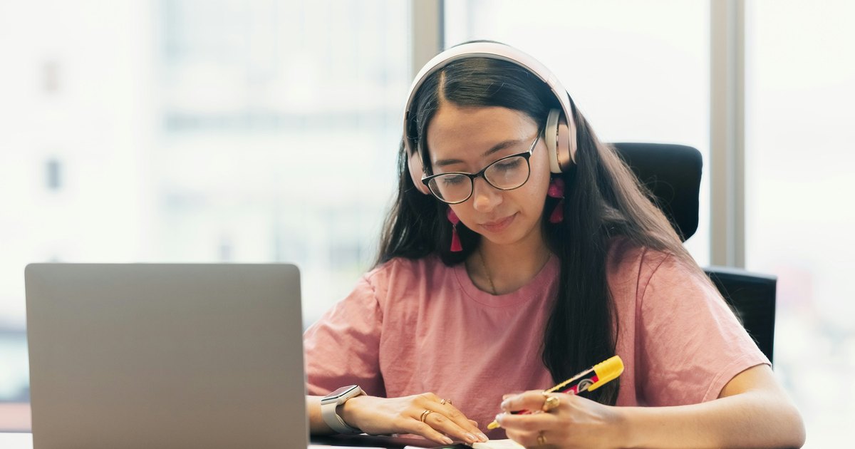Student wearing headphones taking notes during an online German class