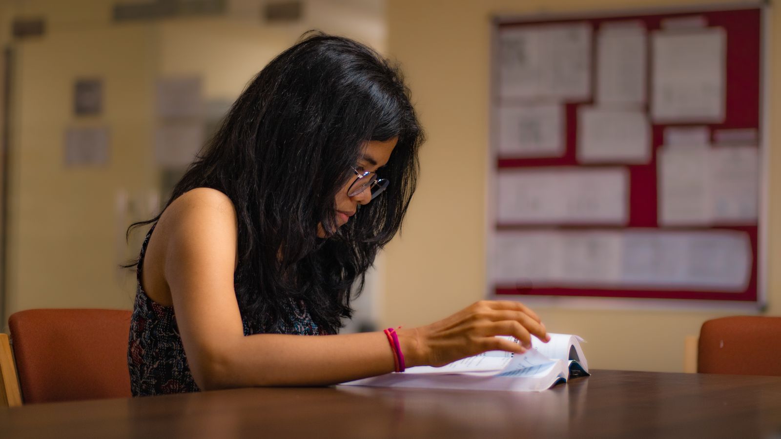 Student reading a textbook at a library desk while preparing for the IELTS exam