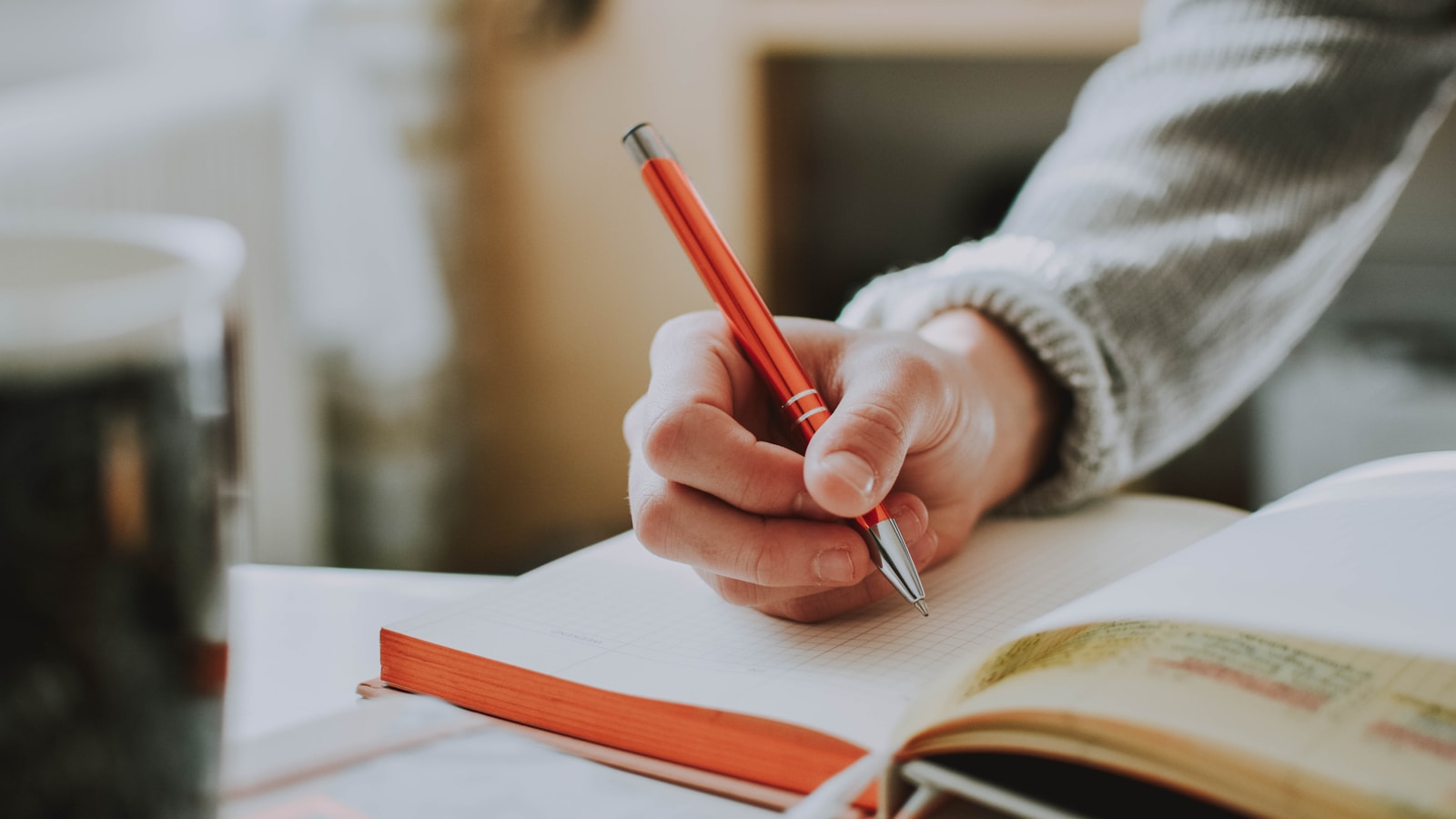 Hand marking written work with a red pen in a notebook, illustrating common IELTS Writing mistakes to correct before the test