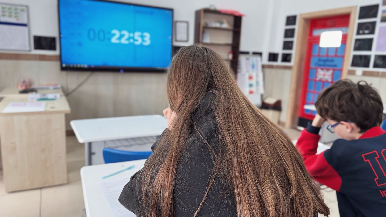 Students sitting a timed IELTS practice test with a countdown clock on the classroom screen